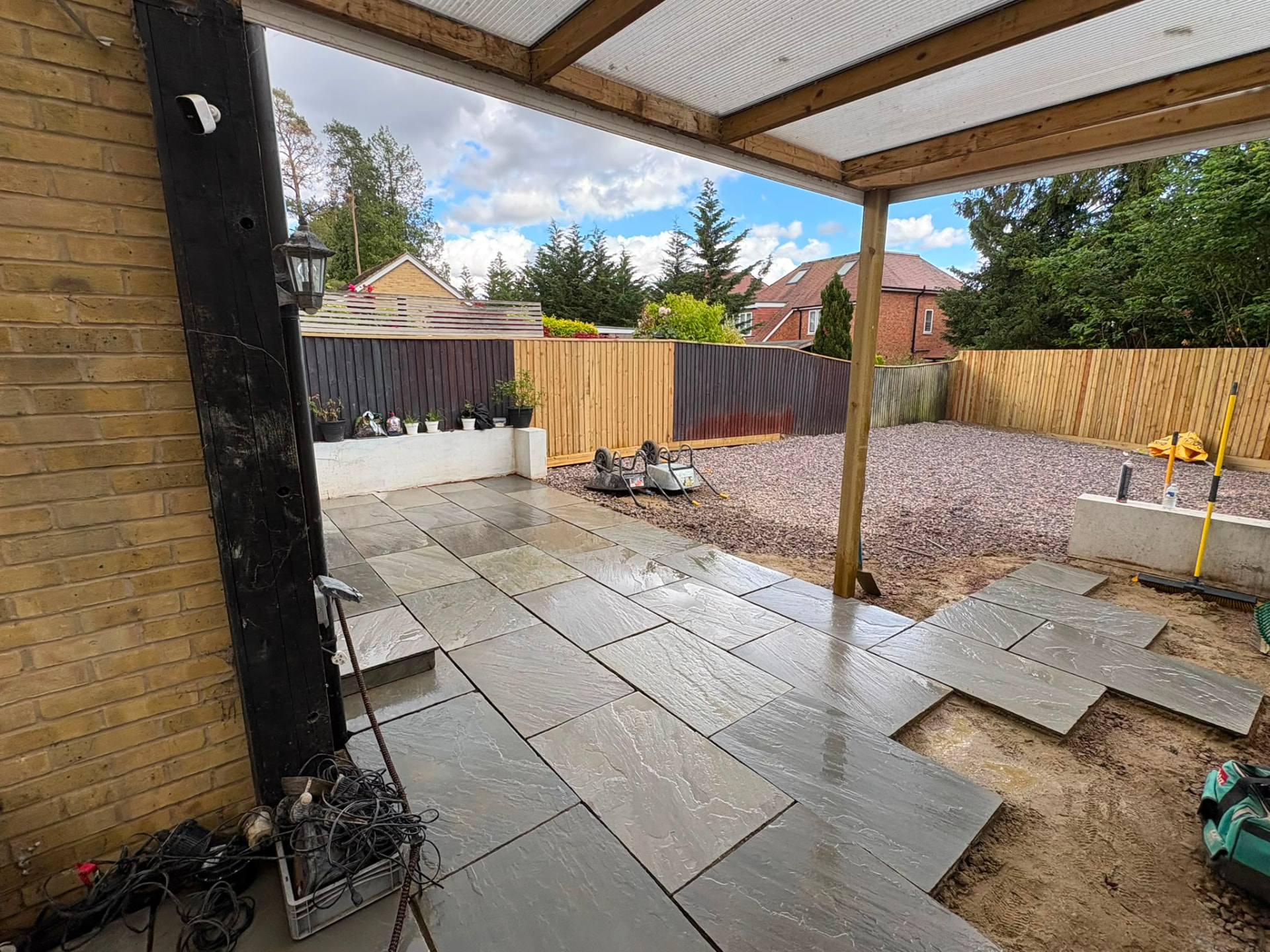 Newly laid grey sandstone patio under a timber and polycarbonate veranda, with new close-board fencing and gravel beds